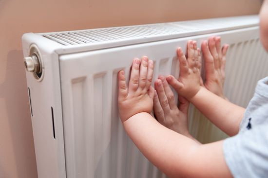 baby-hands-adult-feeling-radiator's-temperature-usually-550nw-12565323b